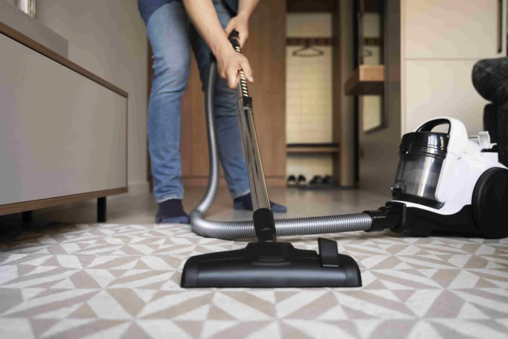 Close-up of a professional vacuuming a light-colored carpet with a modern canister vacuum during commercial carpet cleaning.