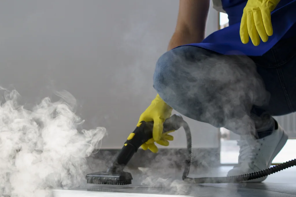 Close-up of a professional using a handheld steam cleaner with heavy steam to remove stains from a carpeted surface.